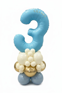 A custom balloon decoration featuring a large light blue number '3' balloon with the name 'OLIVY' printed in gold, supported by a cluster of white, light blue, and metallic gold balloons on a white background.