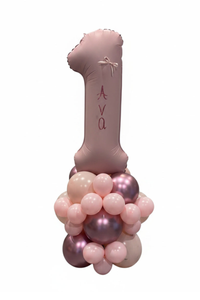 A custom pink foil "1" balloon, personalized with the name 'Ava' in script, supported by a cluster of pink and metallic rose gold balloons on a white background.